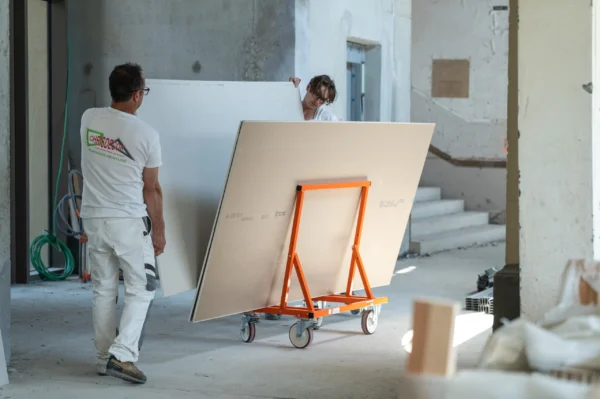 Mondelin 900kg Board Trolley – Operator View Site Handling Tradesmen maneuvering a Mondelin 900kg board trolley loaded with plasterboard panels through a building interior, available for hire at Weller Hire.